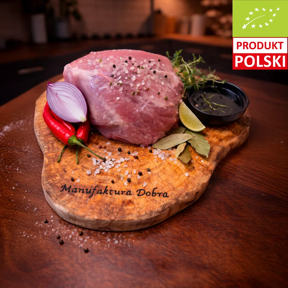 Szynka wieprzowa bez kości EKO z Manufaktury Dobra — surowy kawałek mięsa wieprzowego ze świń rasy puławskiej na tle zielonych liści