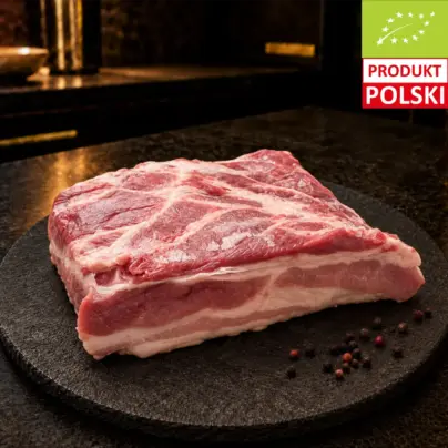 Surowy boczek wieprzowy puławski na czarnej desce, podany z ziarnami pieprzu.
