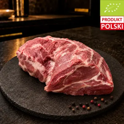 Surowa karkówka wieprzowa na czarnej desce, podana z ziarnami pieprzu.