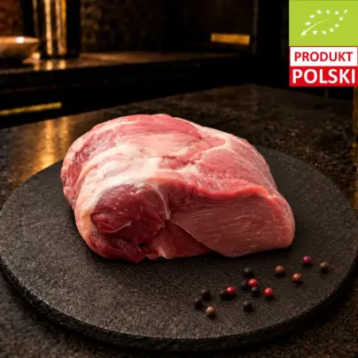 Surowa łopatka wieprzowa puławska na czarnej desce, podana z ziarnami pieprzu.