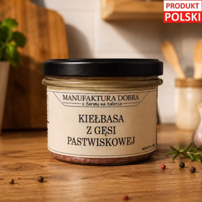 Kiełbasa z gęsi pastwiskowej w szklanym słoiku z etykietą Manufaktura Dobra, na drewnianym blacie z rozmarynem i ziarnami pieprzu w tle