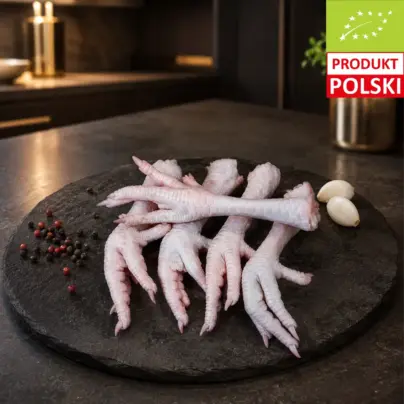 Tekst alternatywny: Surowe łapki z kurczaka pastwiskowego na czarnej desce, z czosnkiem i ziarnami pieprzu.