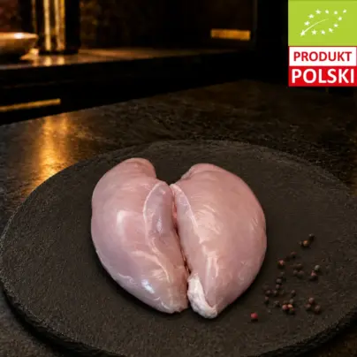 Surowe piersi z kurczaka pastwiskowego na czarnej desce, podane z ziarnami pieprzu.