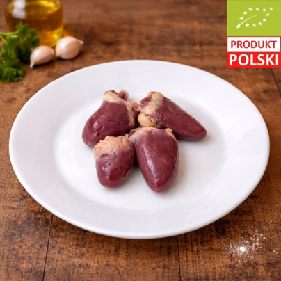 Serca z kurczaka pastwiskowego — cztery surowe serca drobiowe na białym talerzu z ząbkami czosnku, świeżą natką pietruszki i oliwą w tle