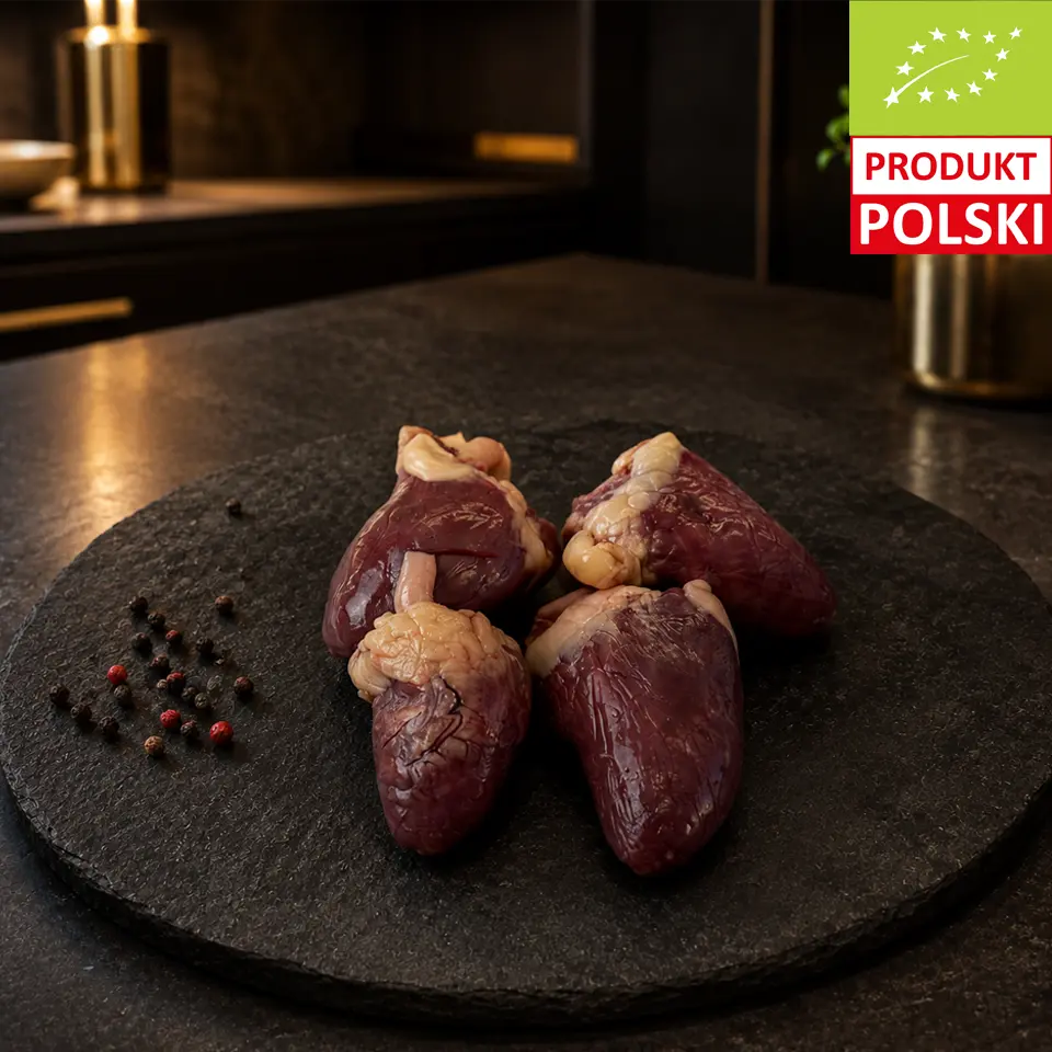 Surowe serca z kurczaka pastwiskowego na czarnej desce, podane z ziarnami pieprzu.