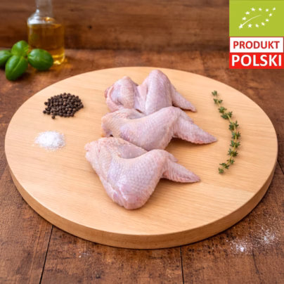 Skrzydełka z kurczaka pastwiskowego — trzy surowe skrzydełka drobiowe ze skórą ułożone na drewnianej desce z pieprzem w ziarnach, solą gruboziarnistą, gałązką tymianku i oliwą w tle