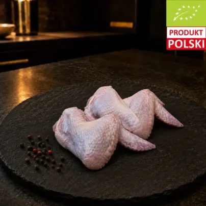 Surowe skrzydełka z kurczaka pastwiskowego na czarnej desce, podane z ziarnami pieprzu.