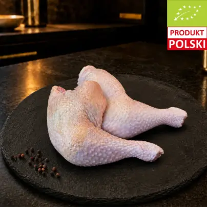 Surowe udka z kurczaka pastwiskowego na czarnej desce, podane z ziarnami pieprzu.
