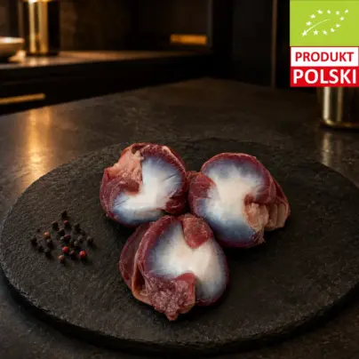 Surowe żołądki z kurczaka pastwiskowego na czarnej desce, podane z ziarnami pieprzu.